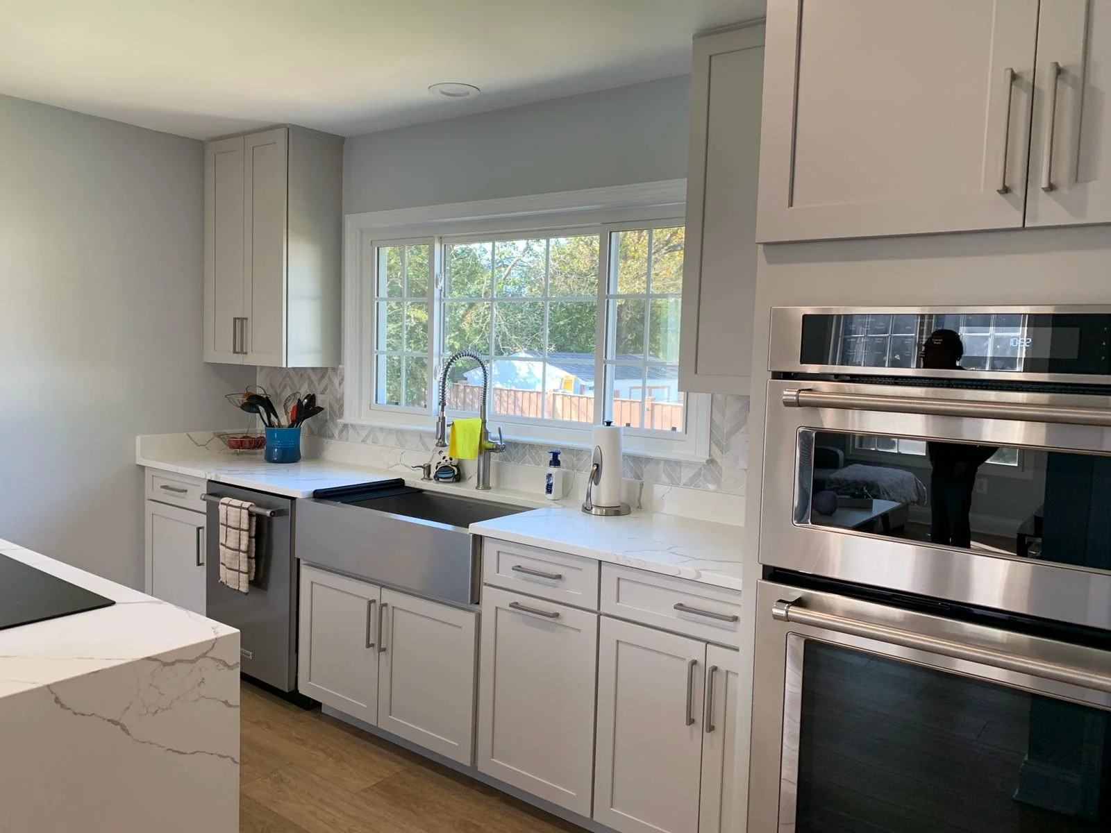 Soft white kitchen with farmhouse sink, double wall ovens and quartz counters