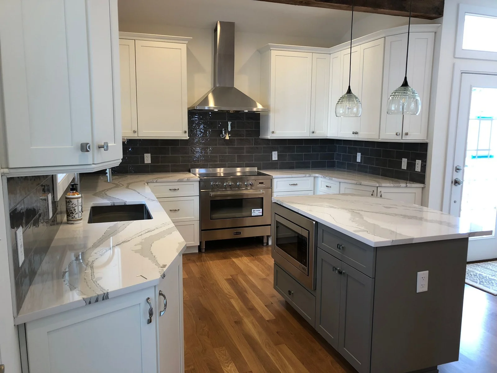 White kitchen with grey island, dark subway backsplash and marble counters