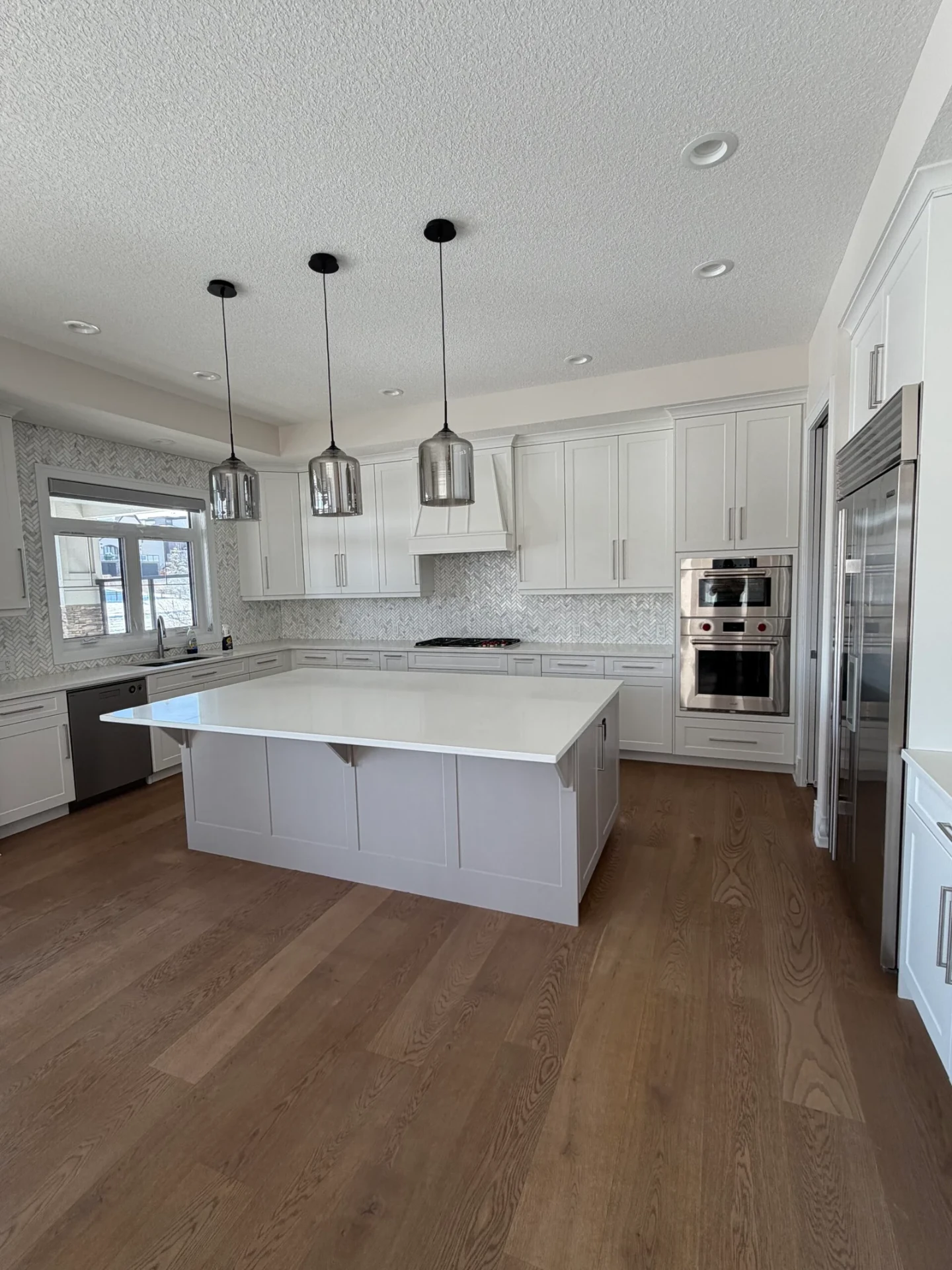 Bright white kitchen with oversized island and herringbone tile backsplash